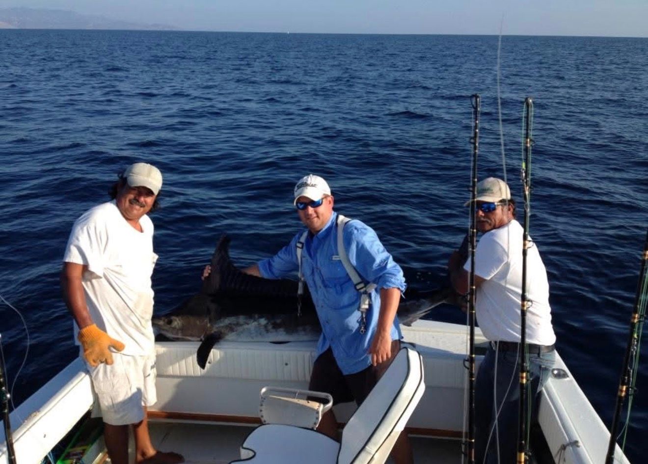Three people on a boat at sea with fishing rods and a large fish on the deck