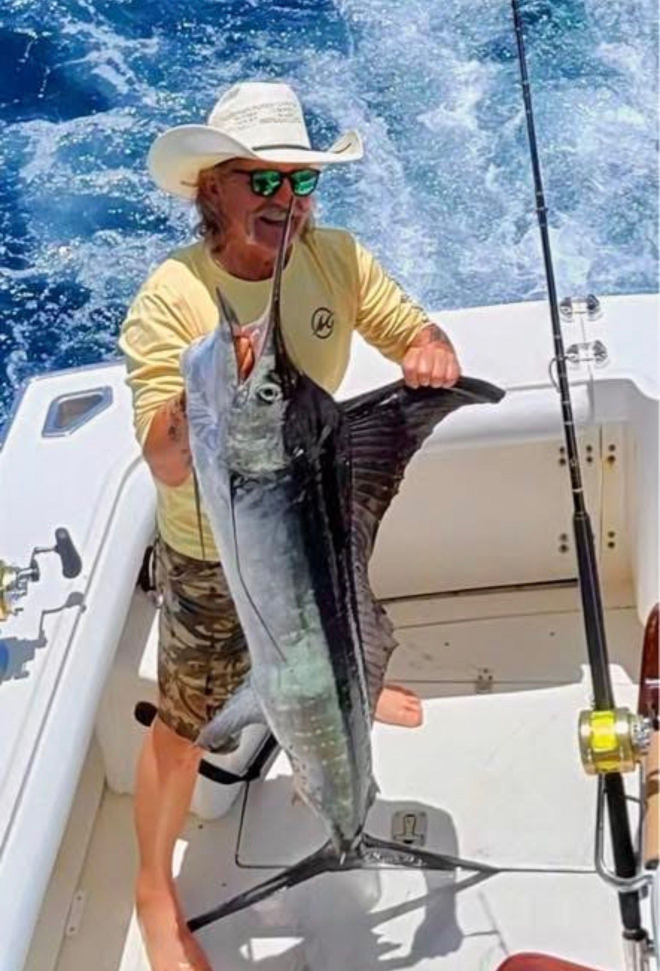 Angler on a boat holding a large swordfish, with blue ocean and fishing rod in the background