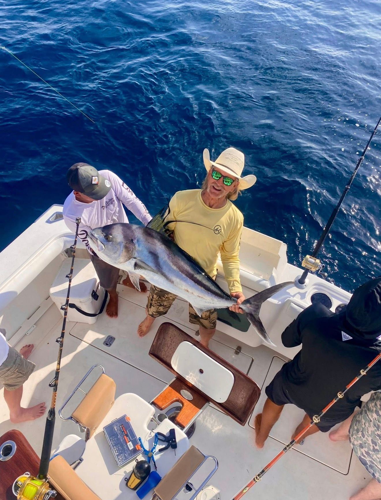 Two anglers on a boat holding a large fish over blue open water.