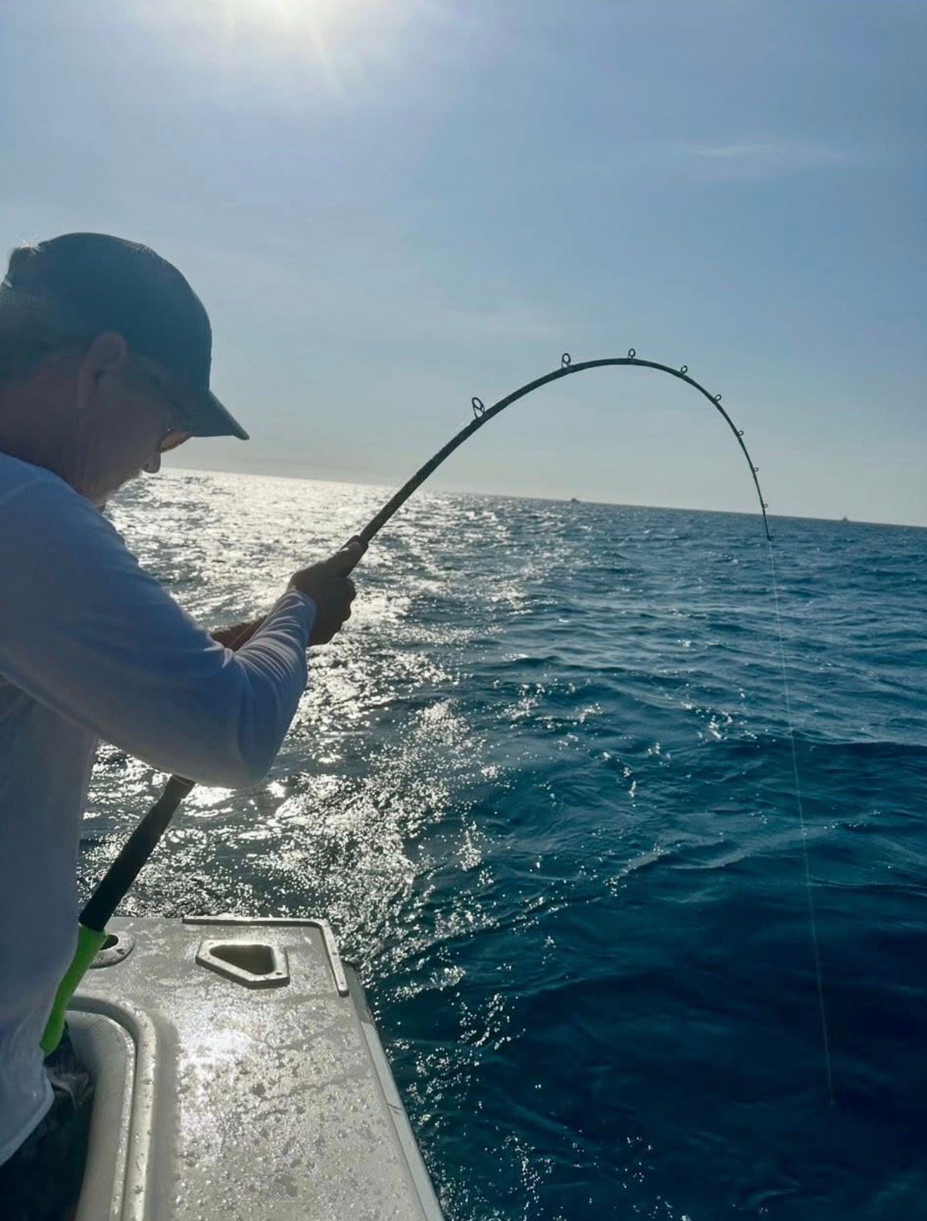 Angler on a boat reels in a fish on a sunny, choppy ocean.
