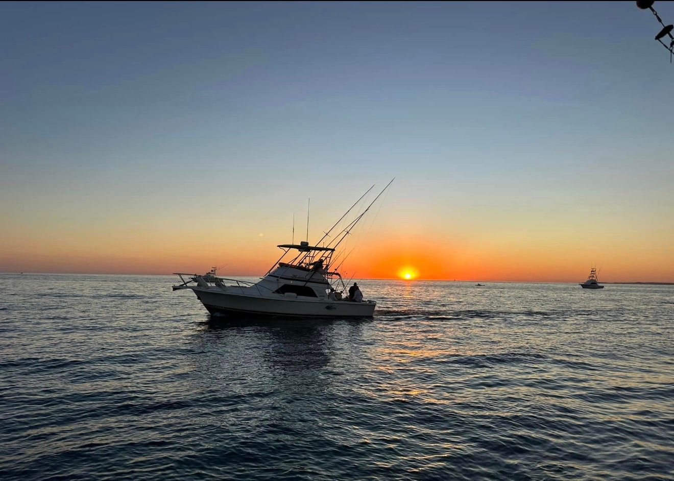 Two fishing boats at sunset on calm water, with silhouetted masts and warm orange sky.