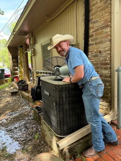 A man in a cowboy hat is standing next to an air conditioner.