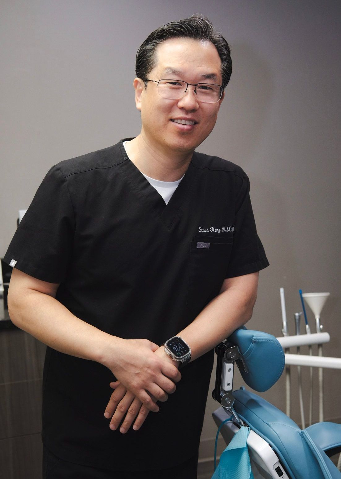 A man in a black scrub is standing in front of a dental chair.