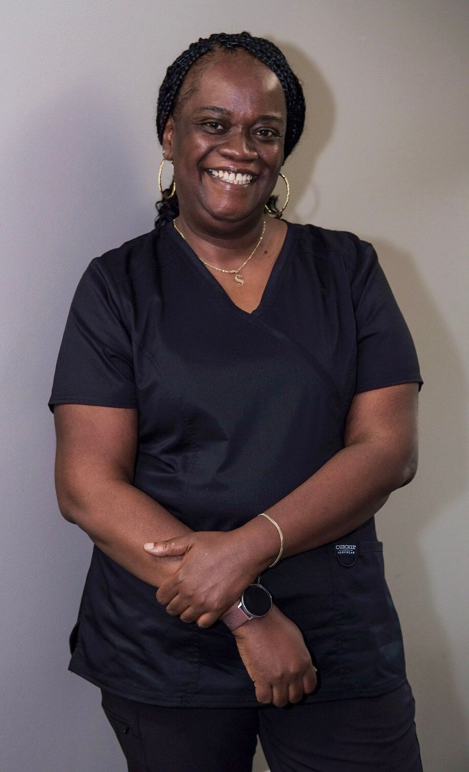 A woman wearing a black scrub top and a necklace is smiling for the camera.