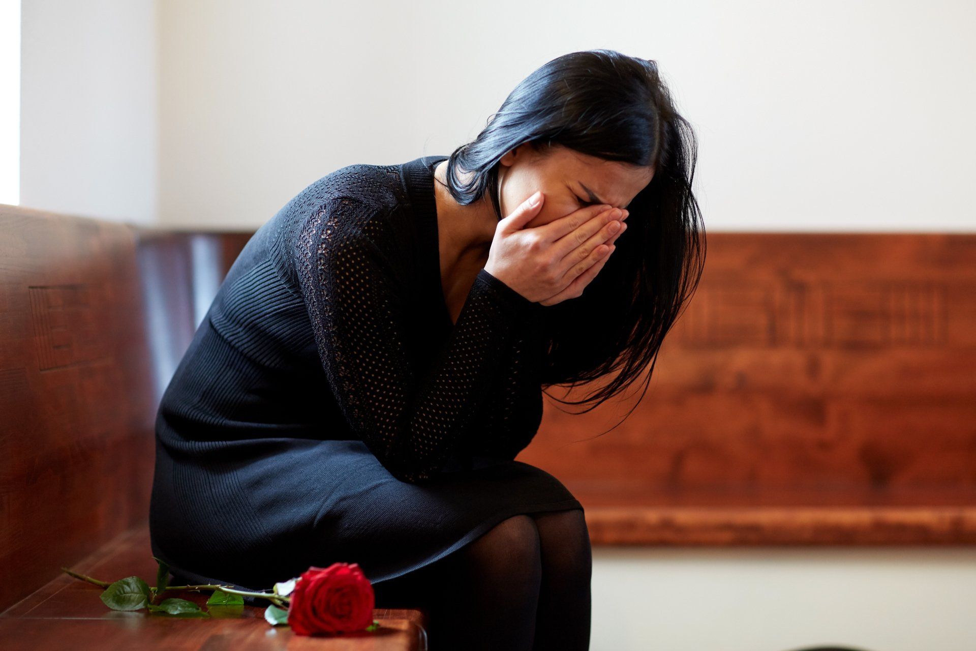 A woman is sitting on a bench with a red rose and crying.