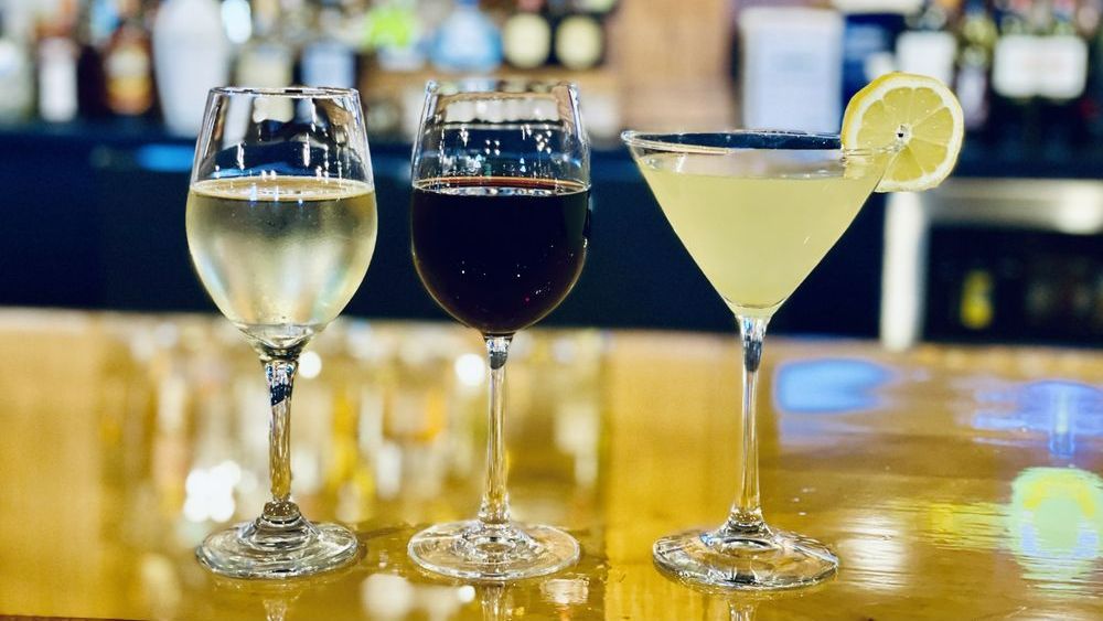 Three glasses of wine and a martini are sitting on a bar.