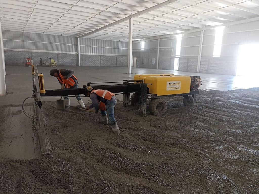 Un grupo de trabajadores de la construcción está trabajando en un piso de concreto en un gran almacén.