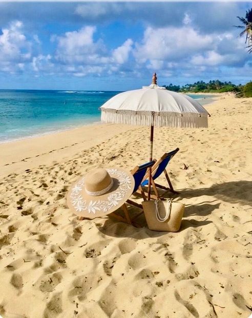 Beach chairs and straw hats under a white umbrella on a sunny tropical beach by the turquoise sea.