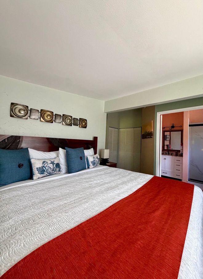 Bedroom with red bed runner, patterned pillows, wall art, and open closet and bathroom doors
