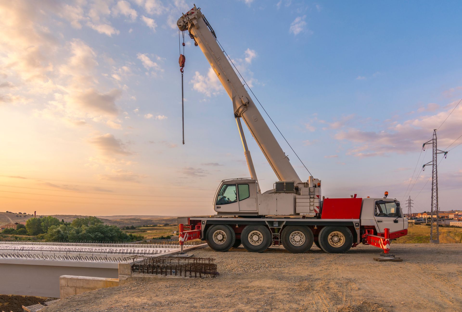 Mobile crane parked at a construction site with its boom raised at sunset.