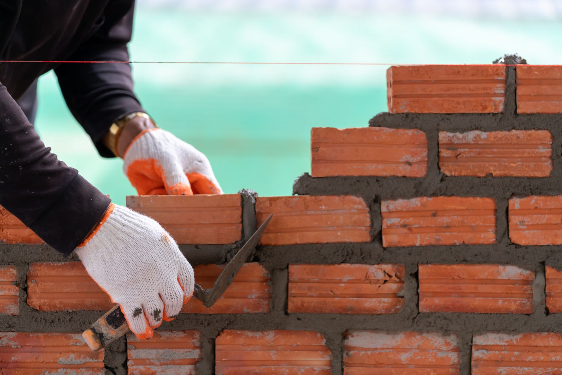 Worker applies mortar between bricks using a trowel, building a straight, level wall.