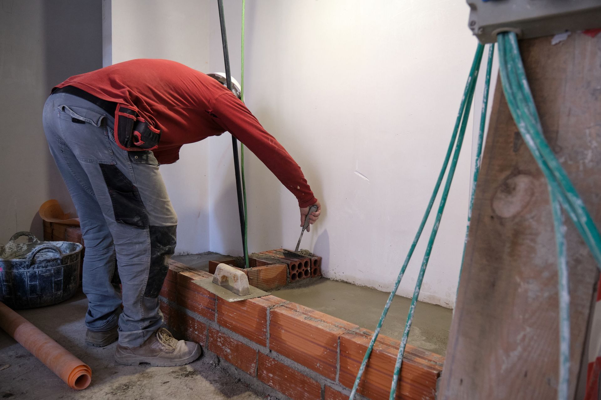 Person adjusts bricks on a wall using tools, surrounded by cement and construction materials. Person adjusts bricks on a wall using tools, surrounded by cement and construction materials.