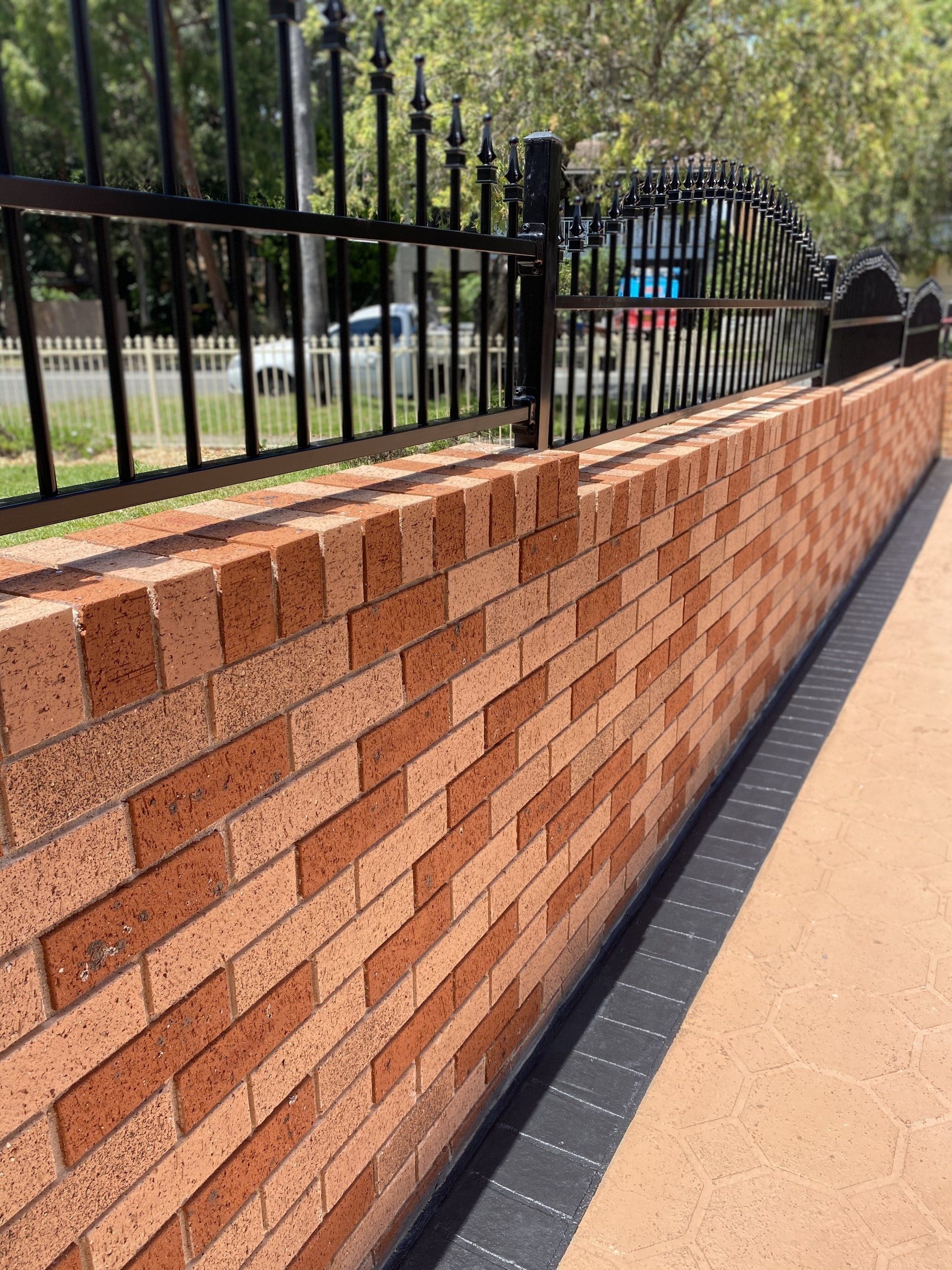 A brick wall with a black fence in the background
