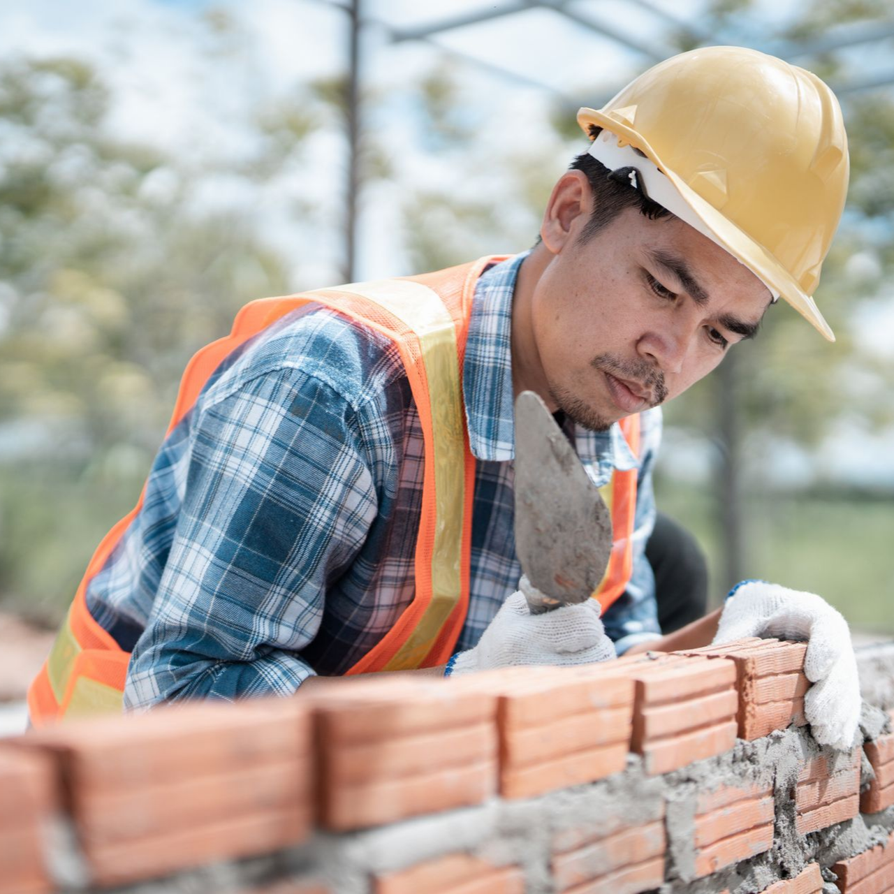 Construction worker performing commercial bricklaying on site wearing safety helmet and vest.