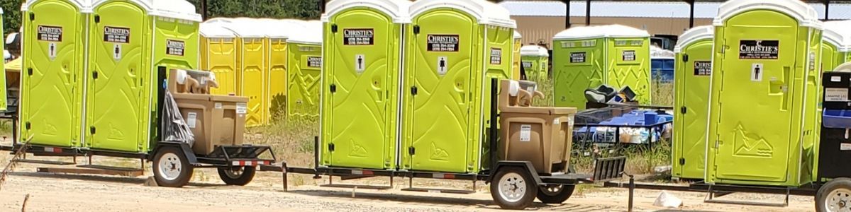 Multiple light green portable toilets mounted on trailers, arranged in rows on a dirt lot.