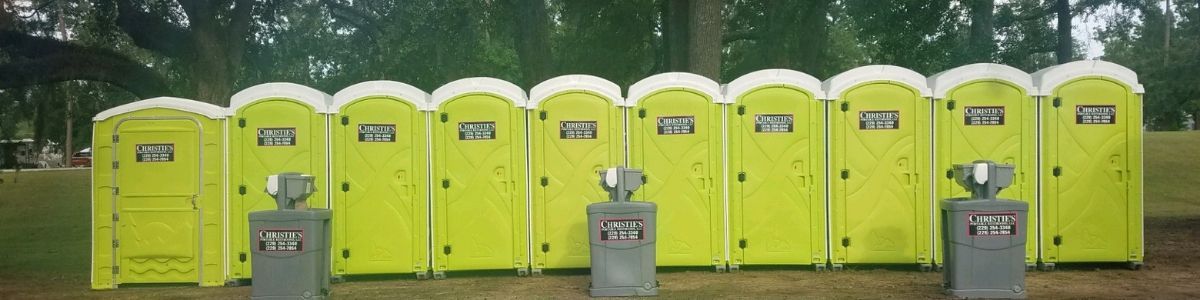 A row of ten bright yellow portable toilets positioned outdoors in a grassy area with three hand-washing stations nearby.