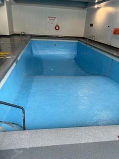 An empty swimming pool with blue water and a life preserver on the wall.