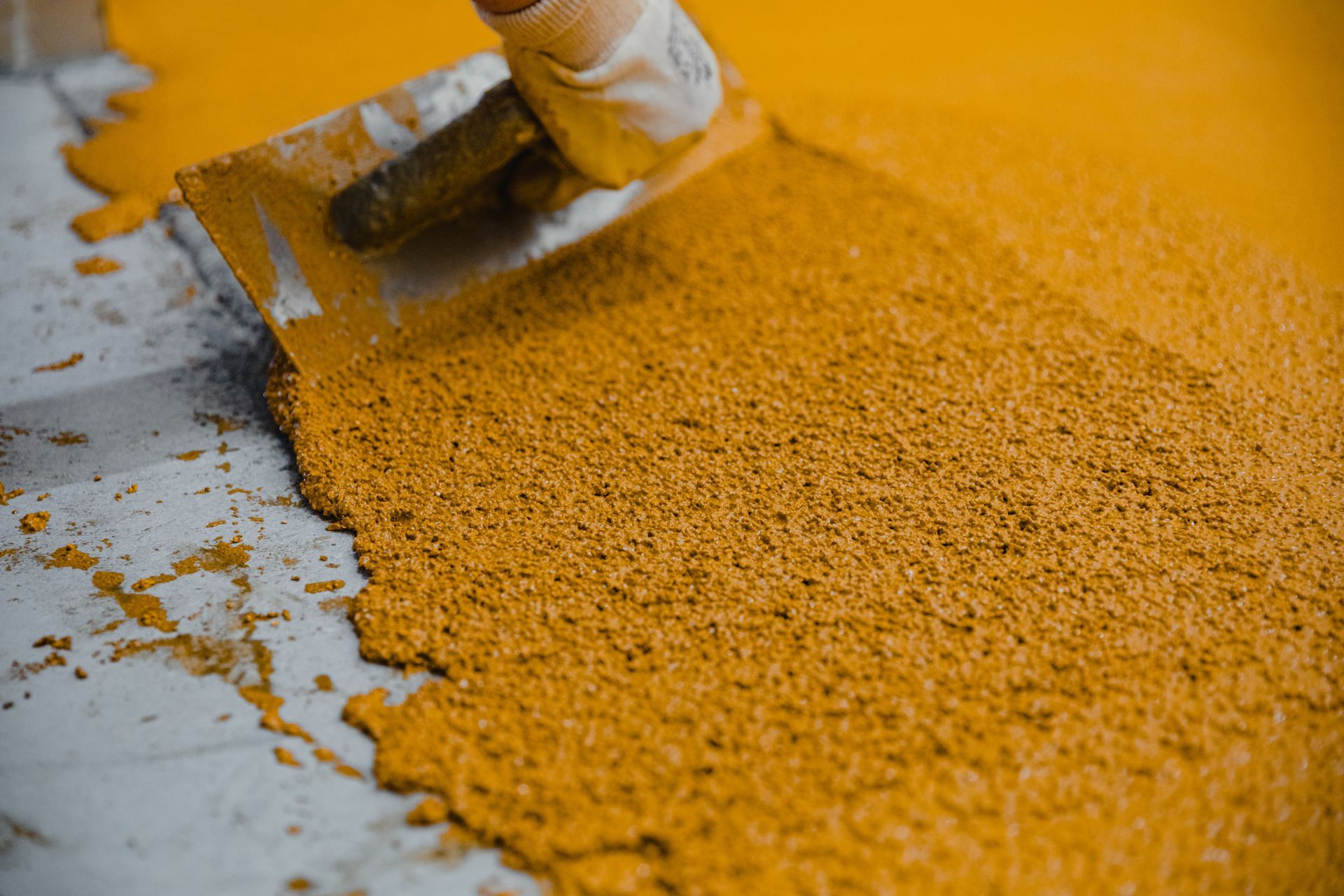 A person is spreading a yellow substance on a floor with a spatula.