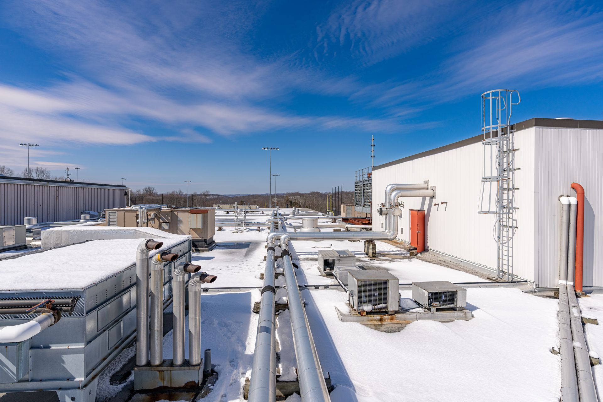 Rooftop with snow, equipment, and a white building against a blue sky with clouds.