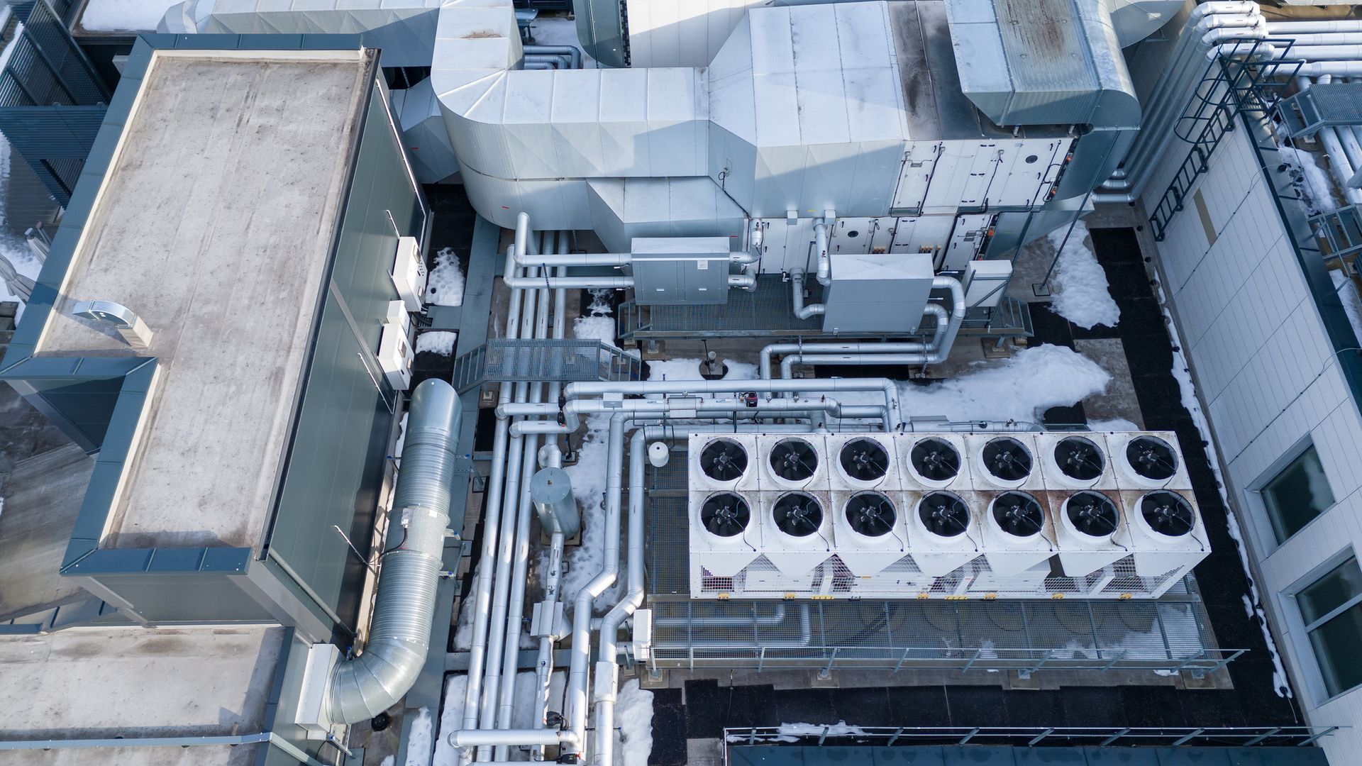 Rooftop HVAC equipment on a commercial building; includes ductwork, air handlers, and cooling units. Snow present.
