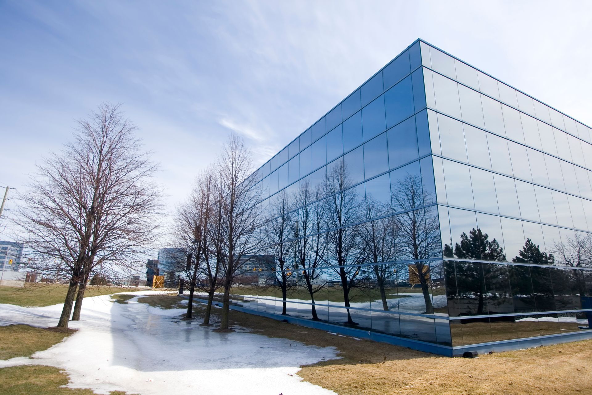 Reflective glass building, blue sky, trees and patchy snow on the ground.