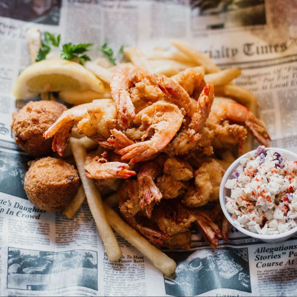 a plate of fried shrimp french fries and coleslaw on a newspaper