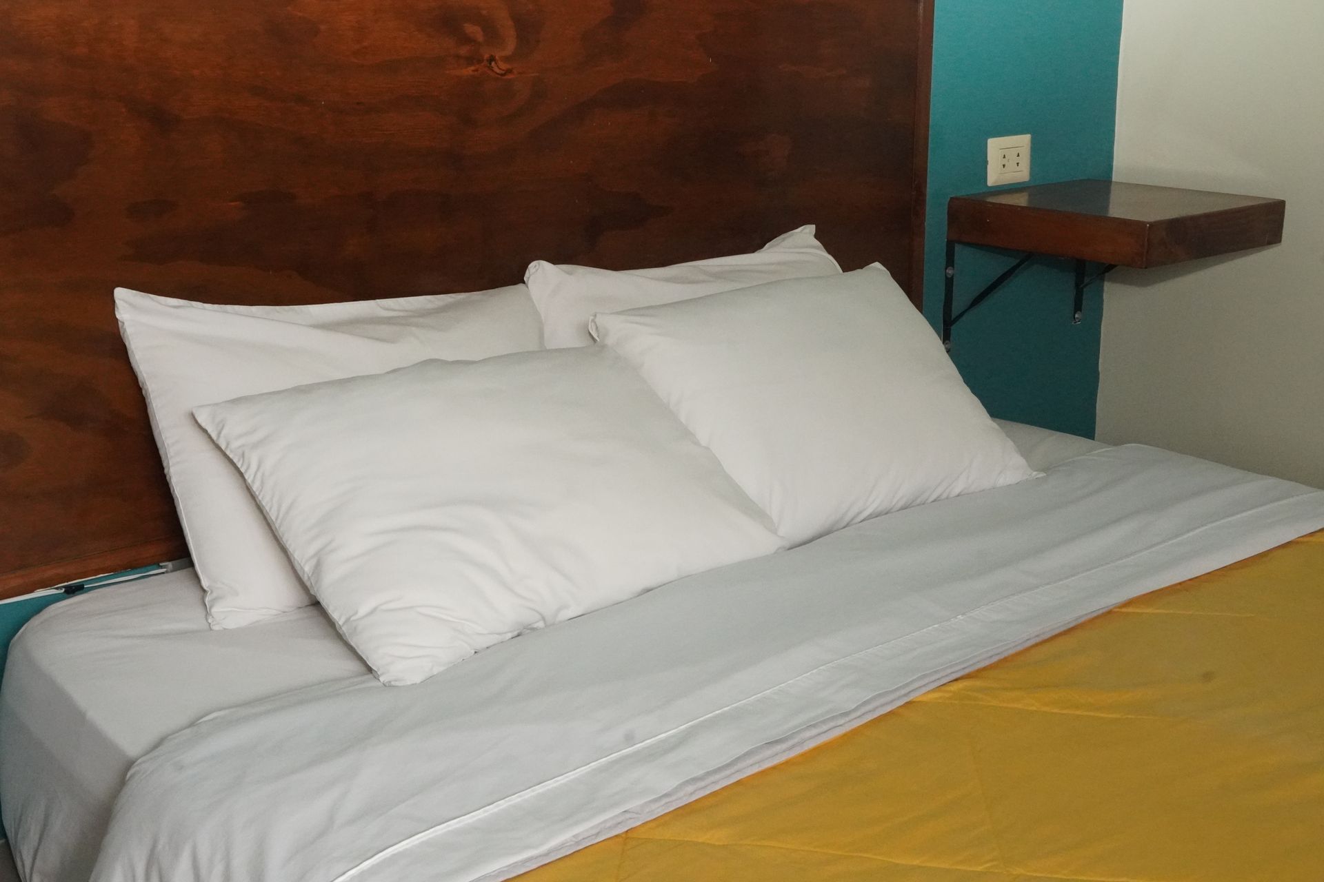 Bed with white pillows and yellow blanket. Dark wood headboard, blue wall, and a small nightstand.