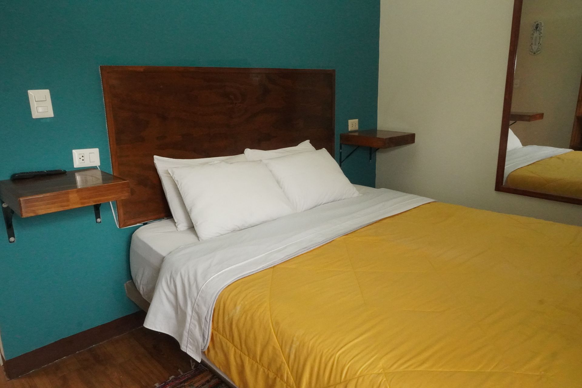Hotel room with bed, wooden headboard, yellow comforter, and turquoise wall.