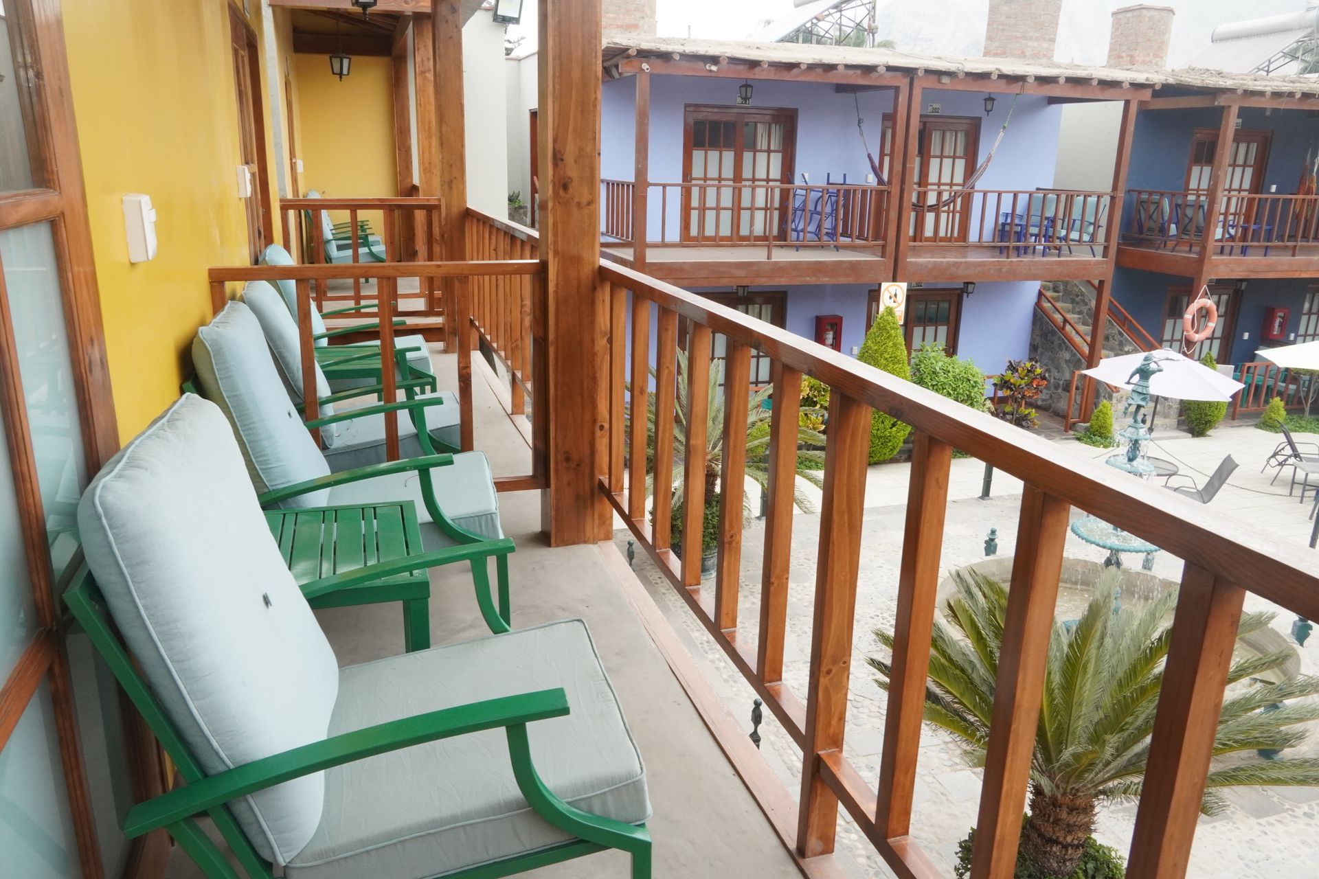 Balcony with chairs overlooking a courtyard of a hotel, with blue and yellow buildings.
