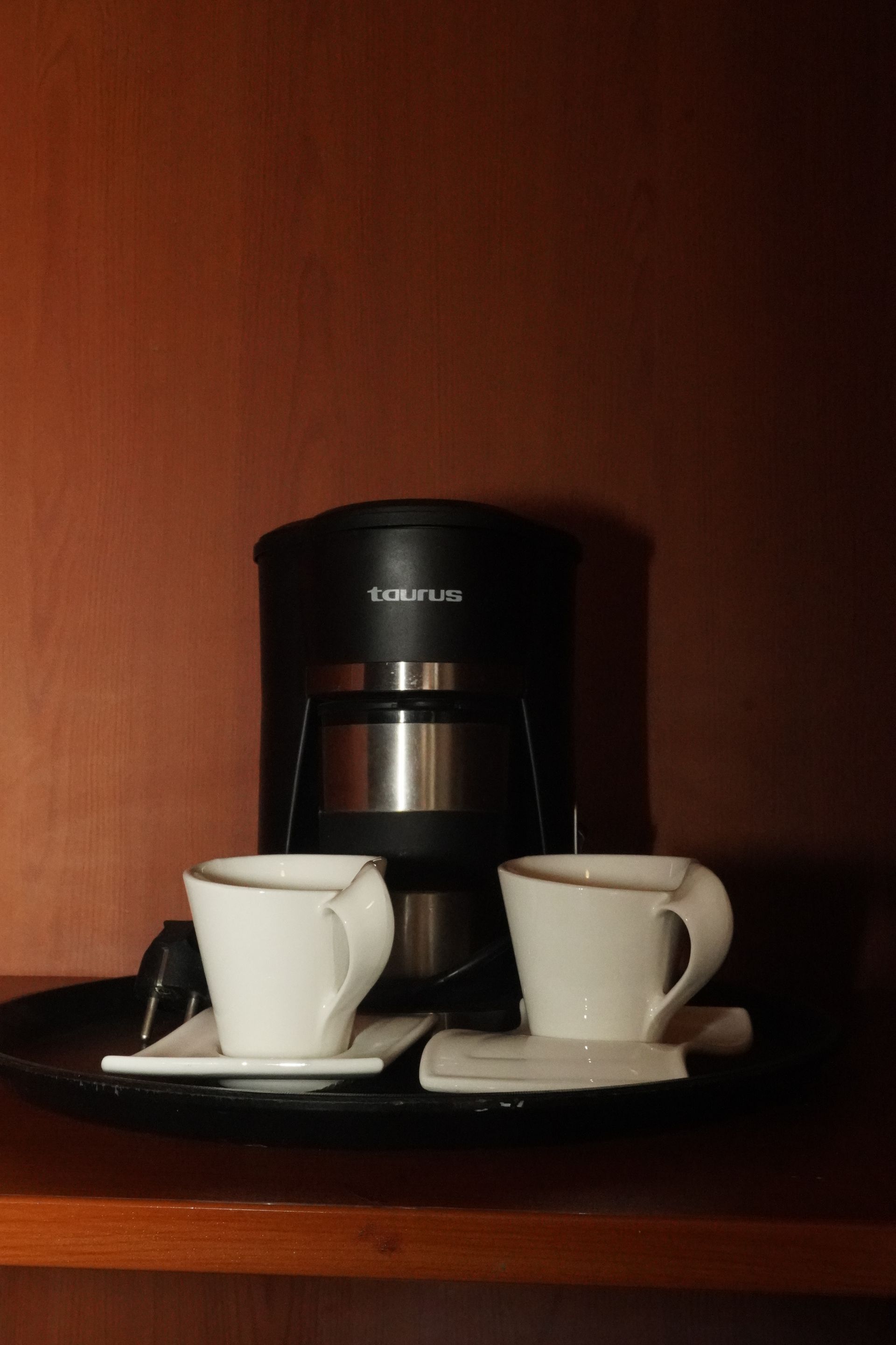 Coffee maker with two white coffee cups on a tray. Dark brown background.