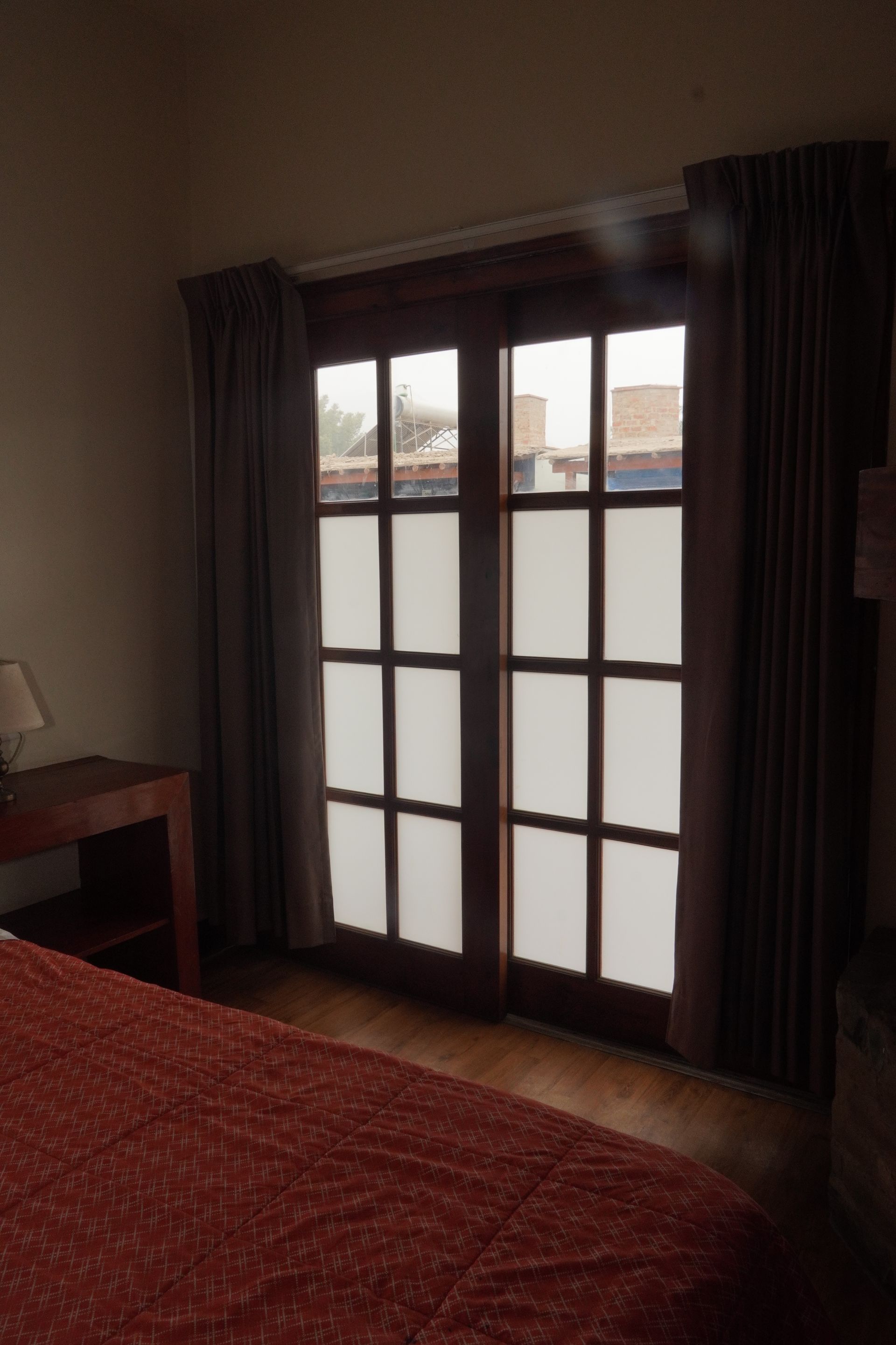 Bedroom with wooden French doors, sheer window coverings, and burgundy curtains.