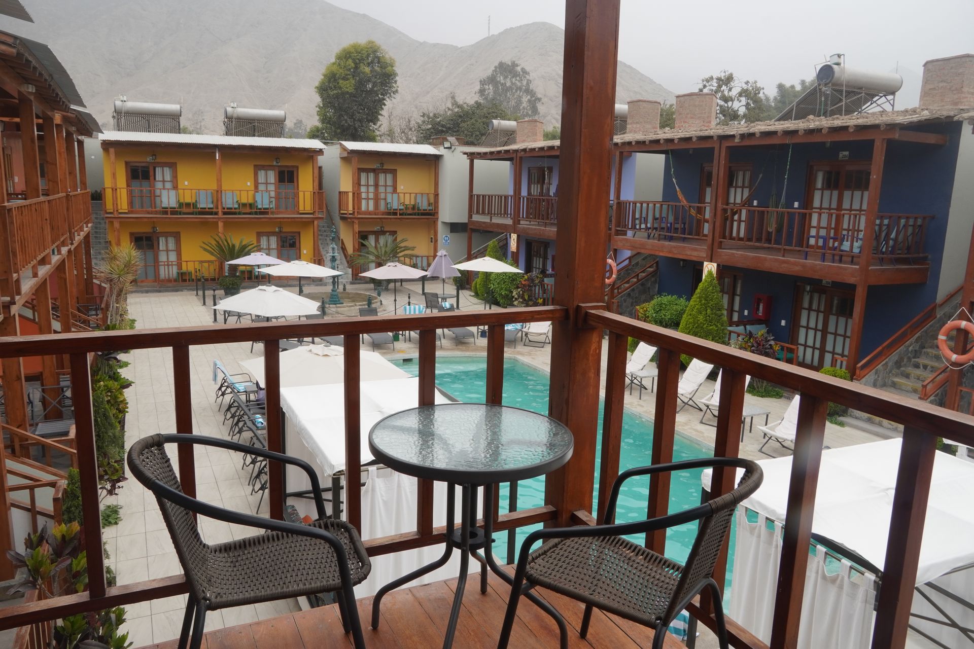 Balcony view of a resort courtyard with a pool, tables, and colorful buildings.