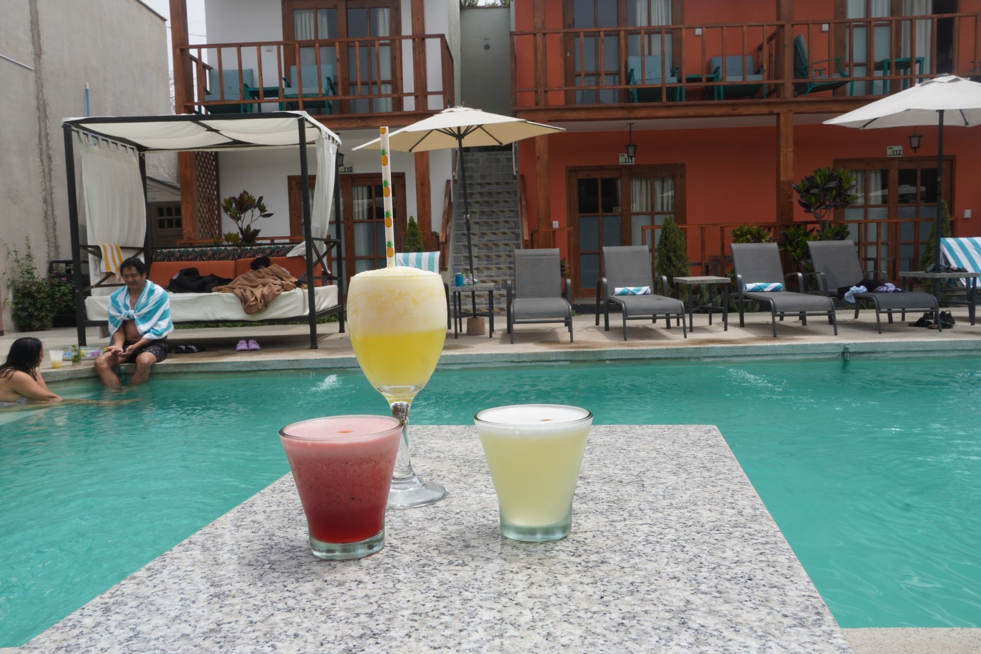 Desk with wooden trestle legs, a wood and black chair, and a white lamp against a white wall with sunlit window shadows.