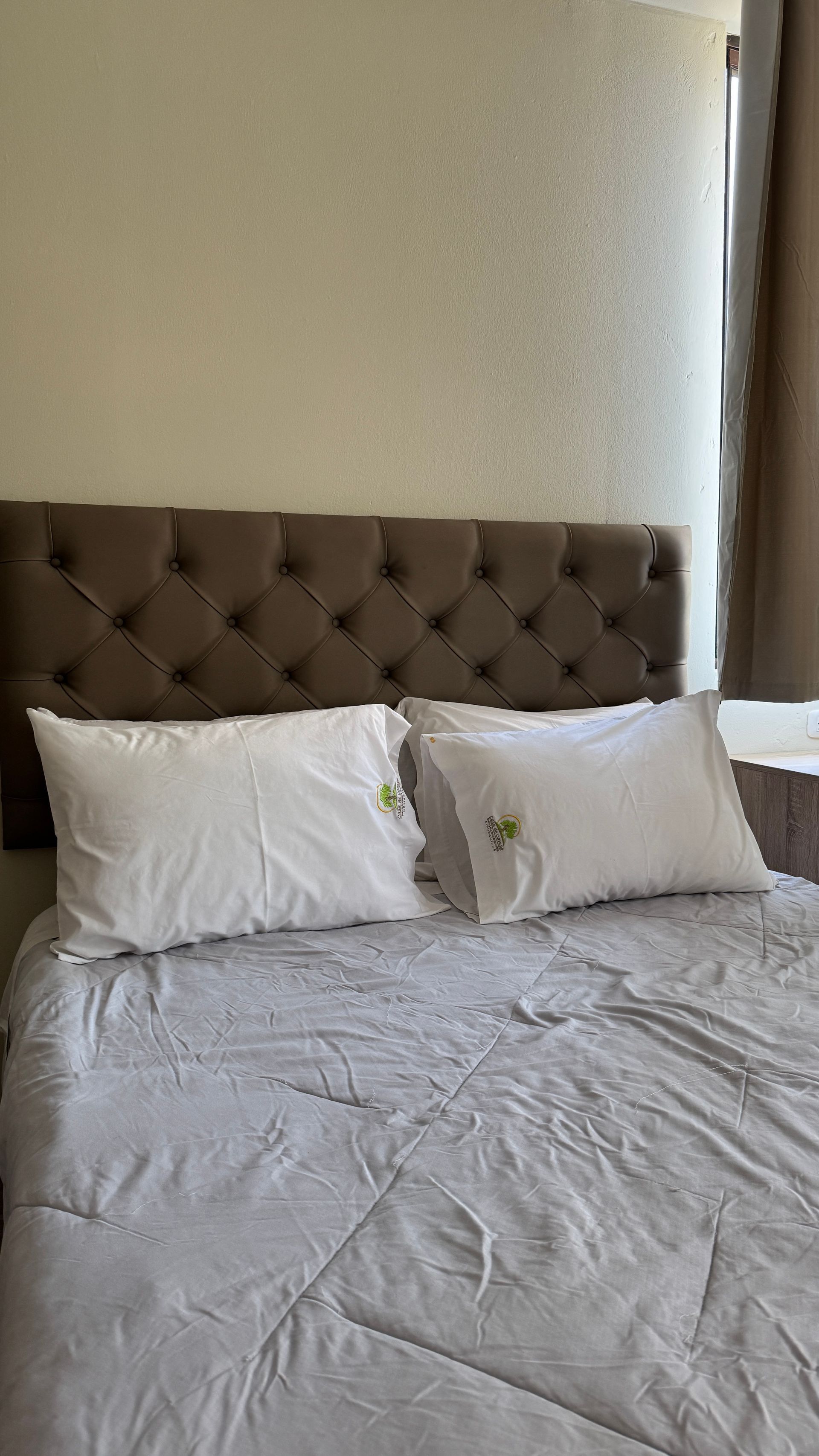 Bed with white pillows and a button-tufted brown headboard. Gray comforter.