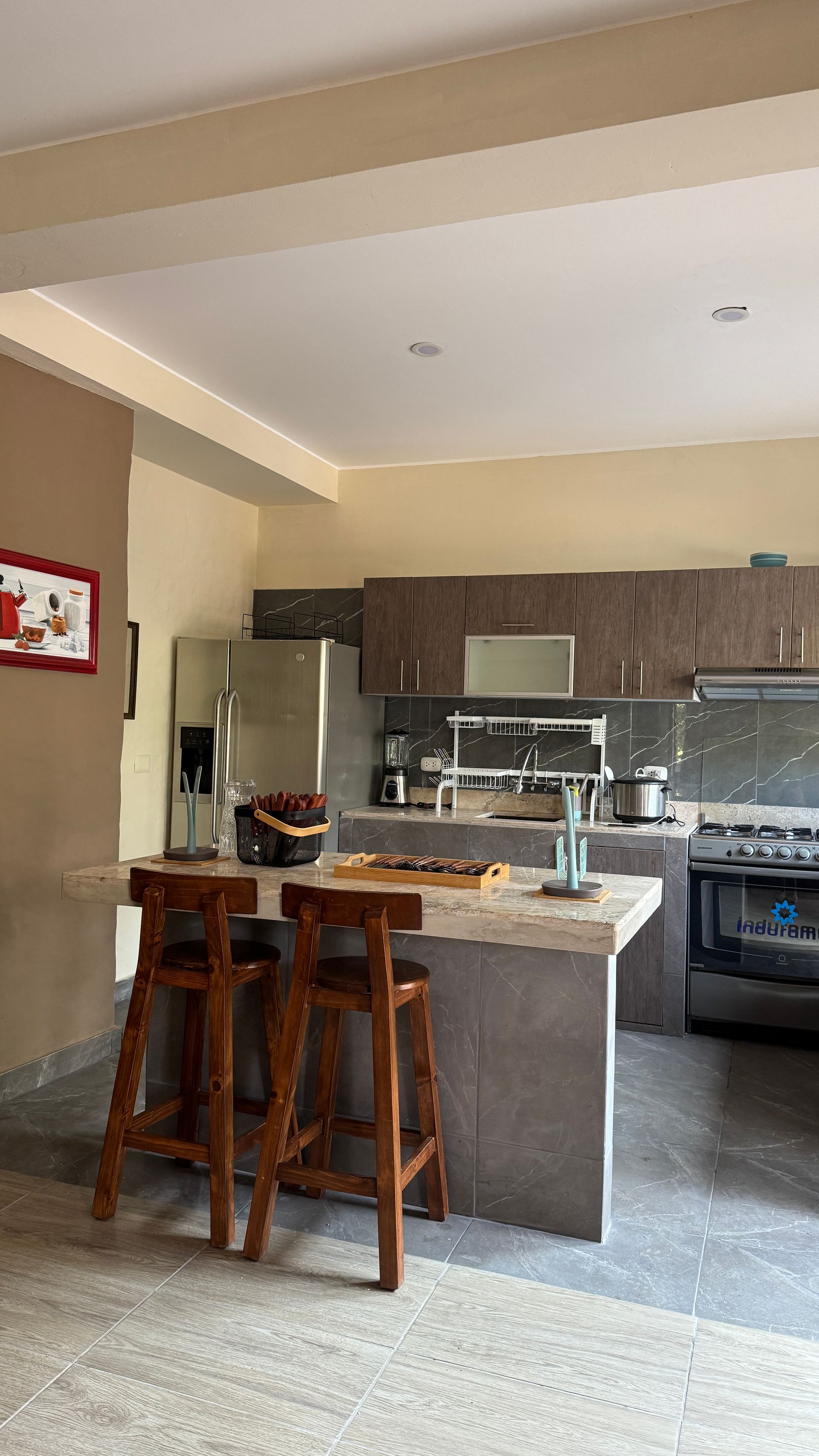 Kitchen with a gray island, wooden stools, stainless steel appliances, and dark brown cabinets.