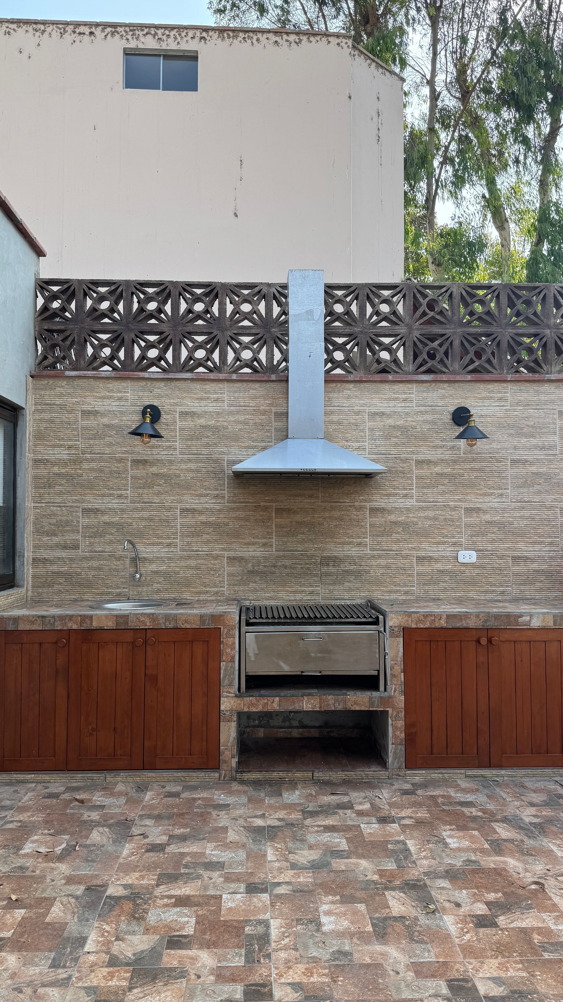 Outdoor kitchen with a brick backdrop, grill, hood, and wooden cabinets.