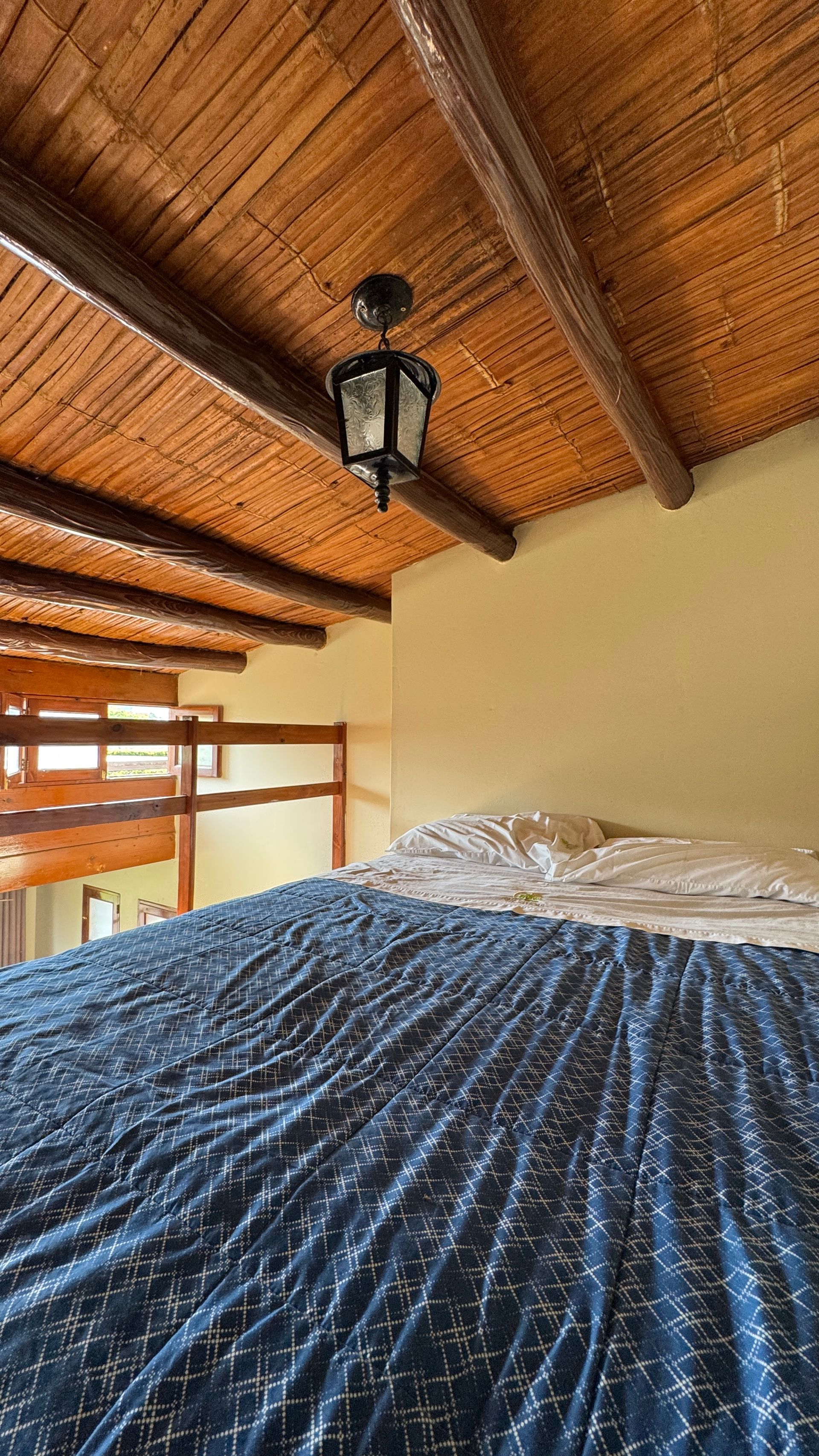 Bed in a room with a bamboo ceiling, decorative light fixture, and wooden beams.