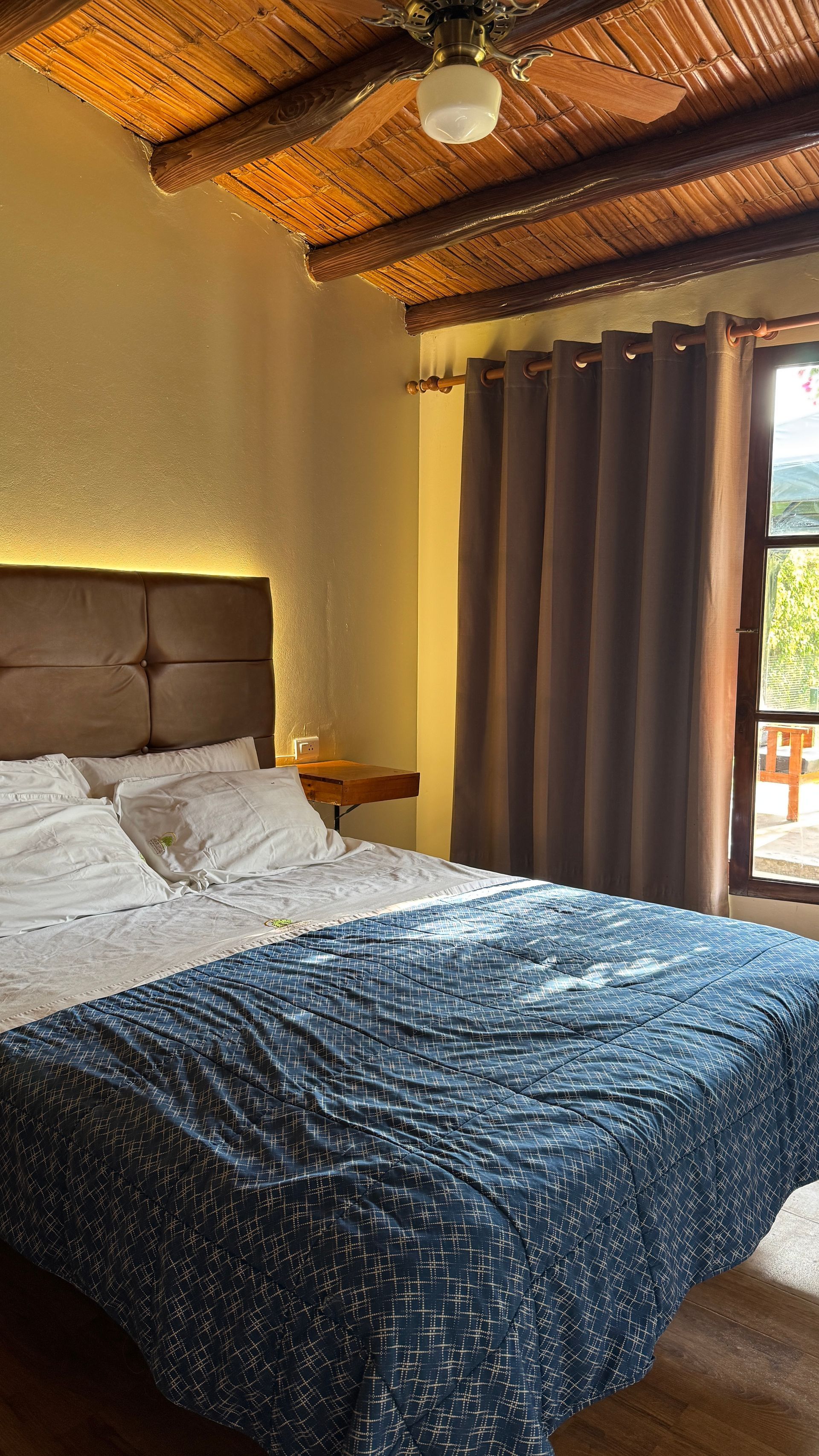Bedroom with a blue comforter on the bed, brown curtains, and a wooden ceiling.