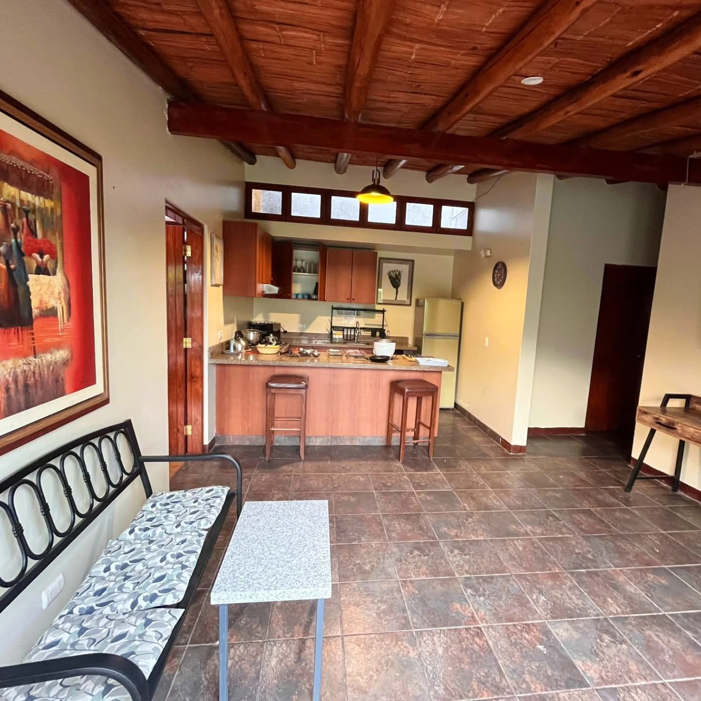 Cozy kitchen and living area with wood ceiling and tiled floor. Features include a bar, cabinets, and a painting.