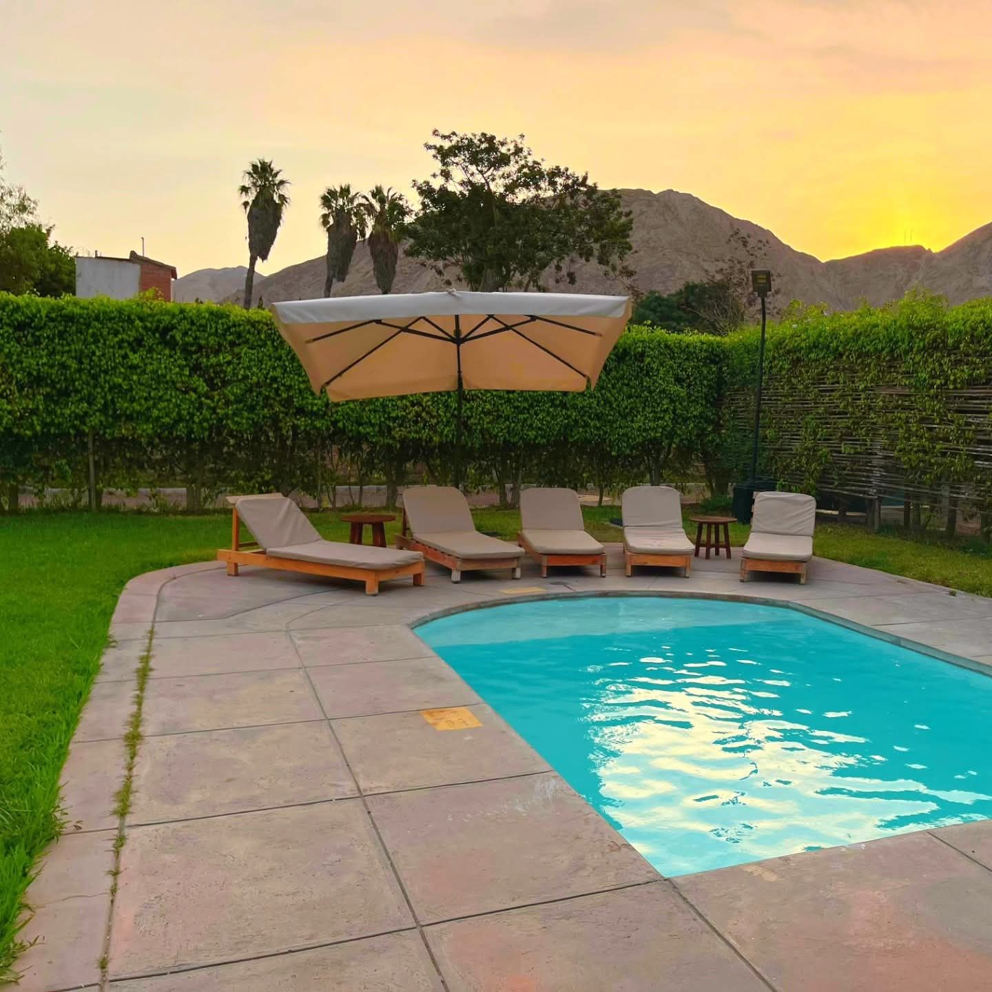 Swimming pool with lounge chairs, umbrella, and mountain backdrop at sunset.