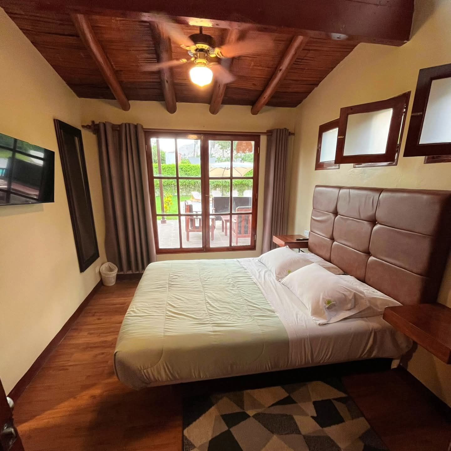 Bedroom with a double bed, wooden ceiling, and large window overlooking an outdoor patio.