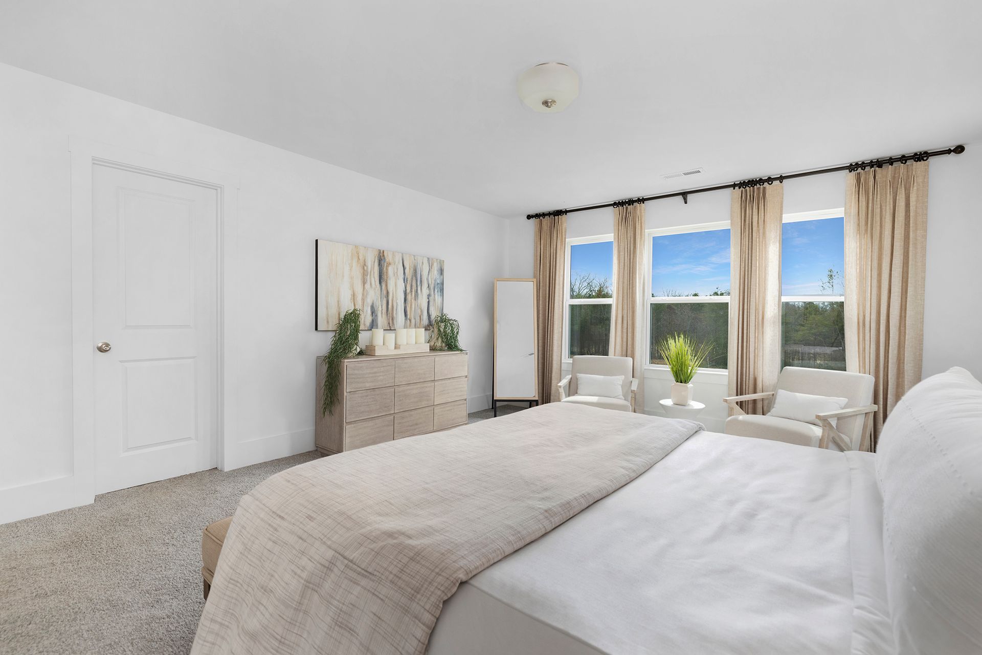 A bedroom with a large bed , dresser , chairs and windows.