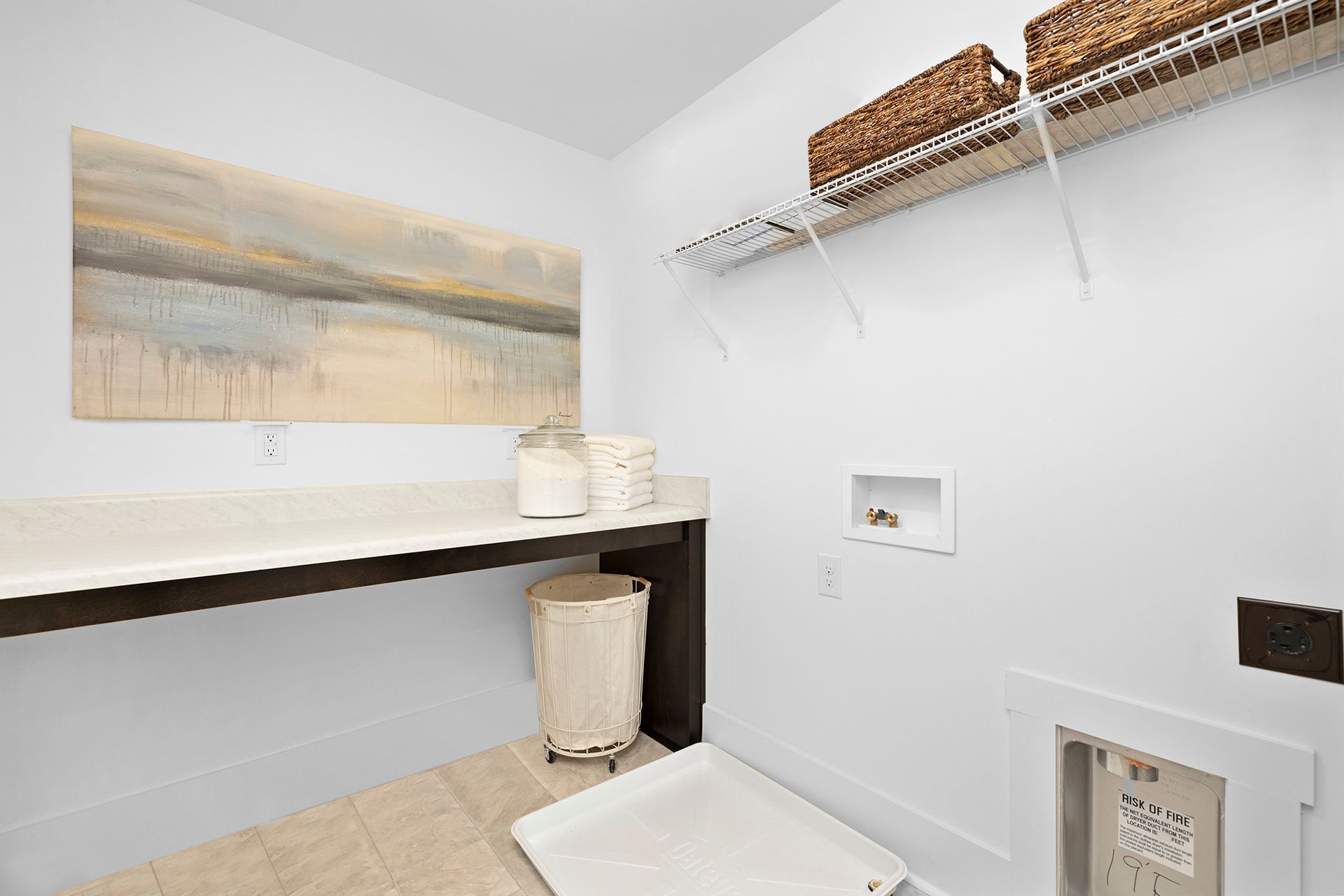 A laundry room with a table , baskets , and a painting on the wall.