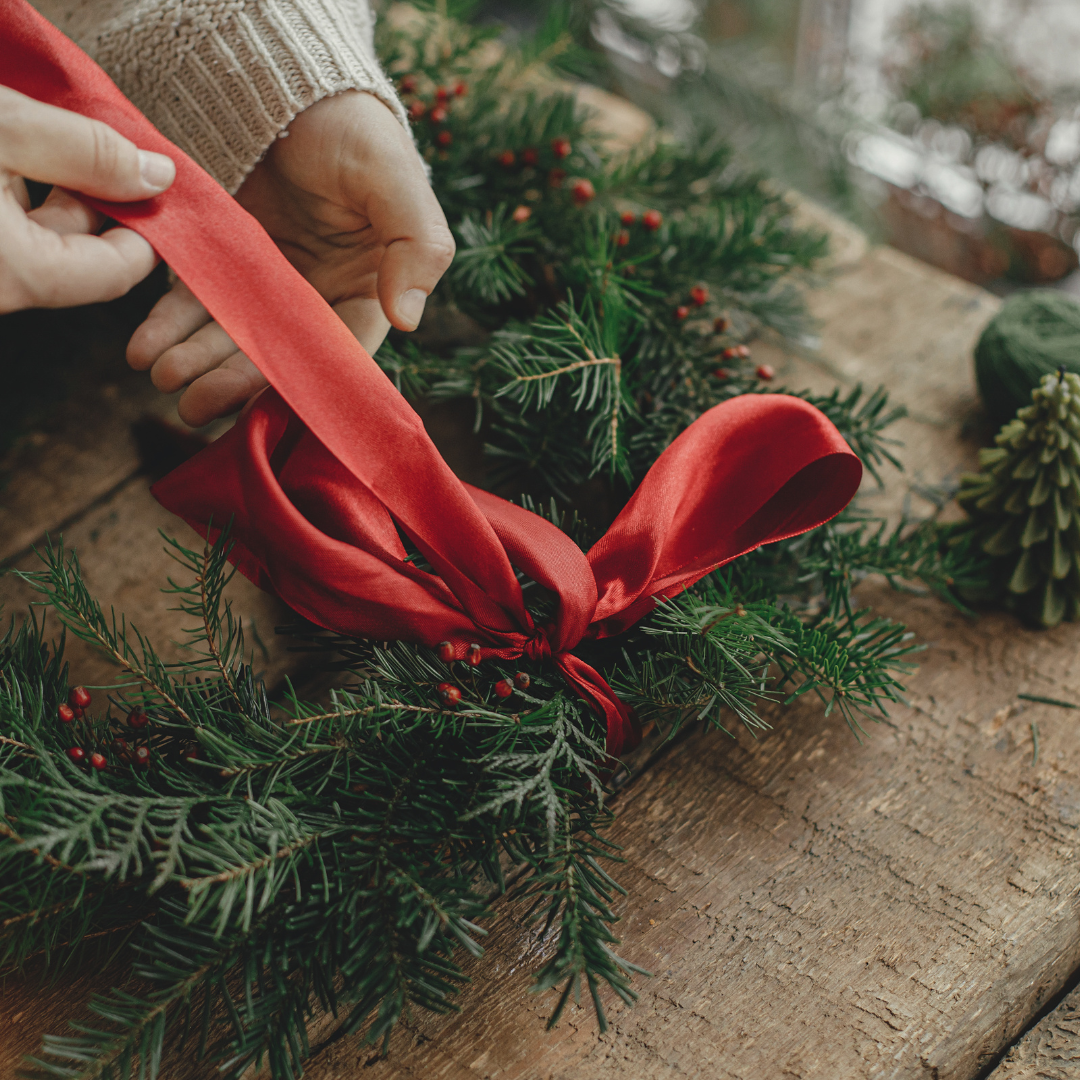 a person is tying a red ribbon around a christmas wreath .