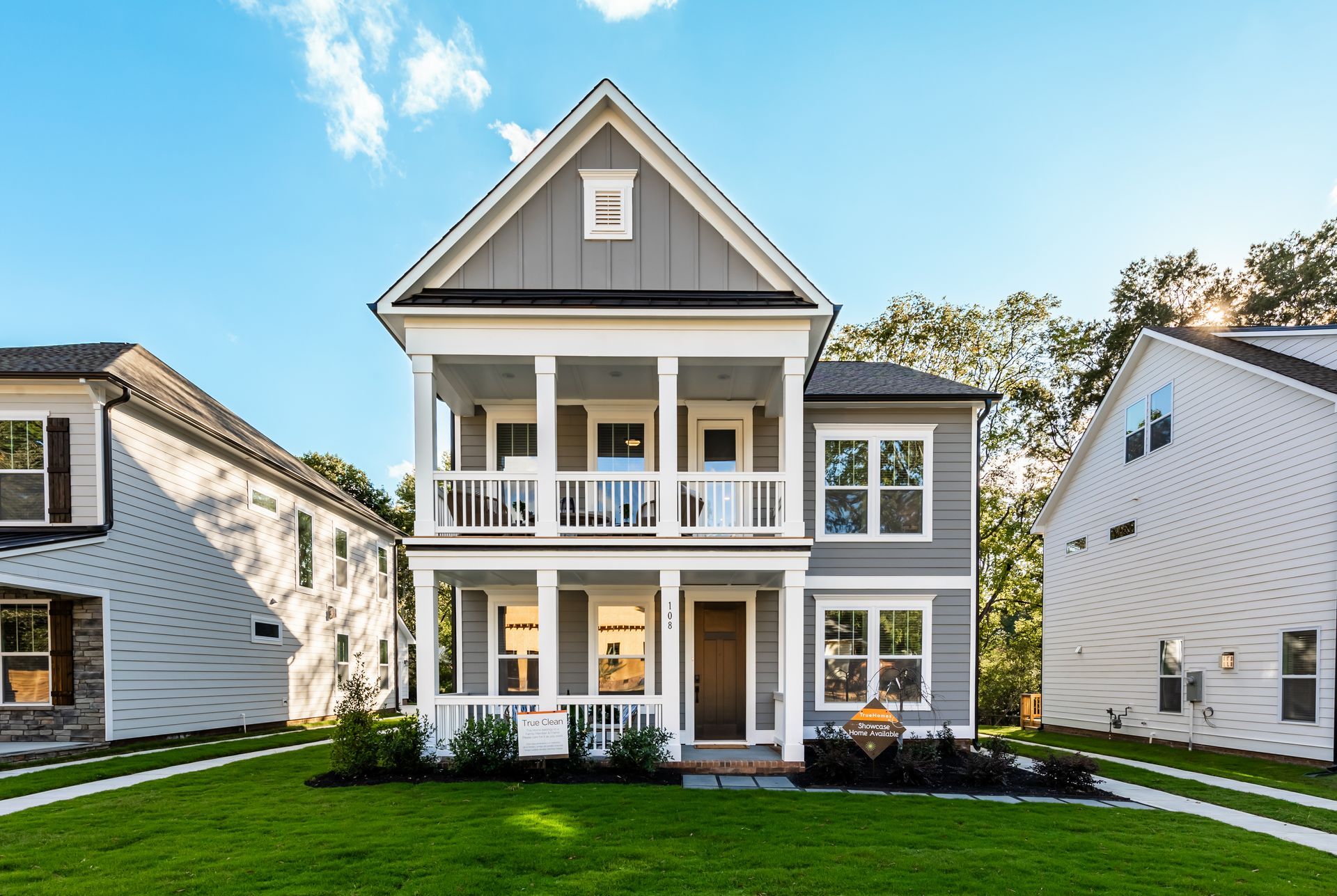 a large gray and white house with a large porch is sitting on top of a lush green lawn .