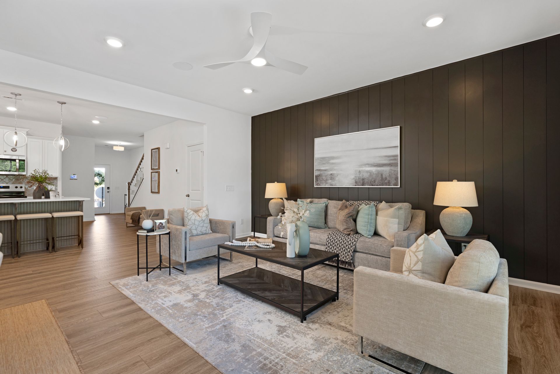A living room with a couch , two chairs , a coffee table and a ceiling fan.