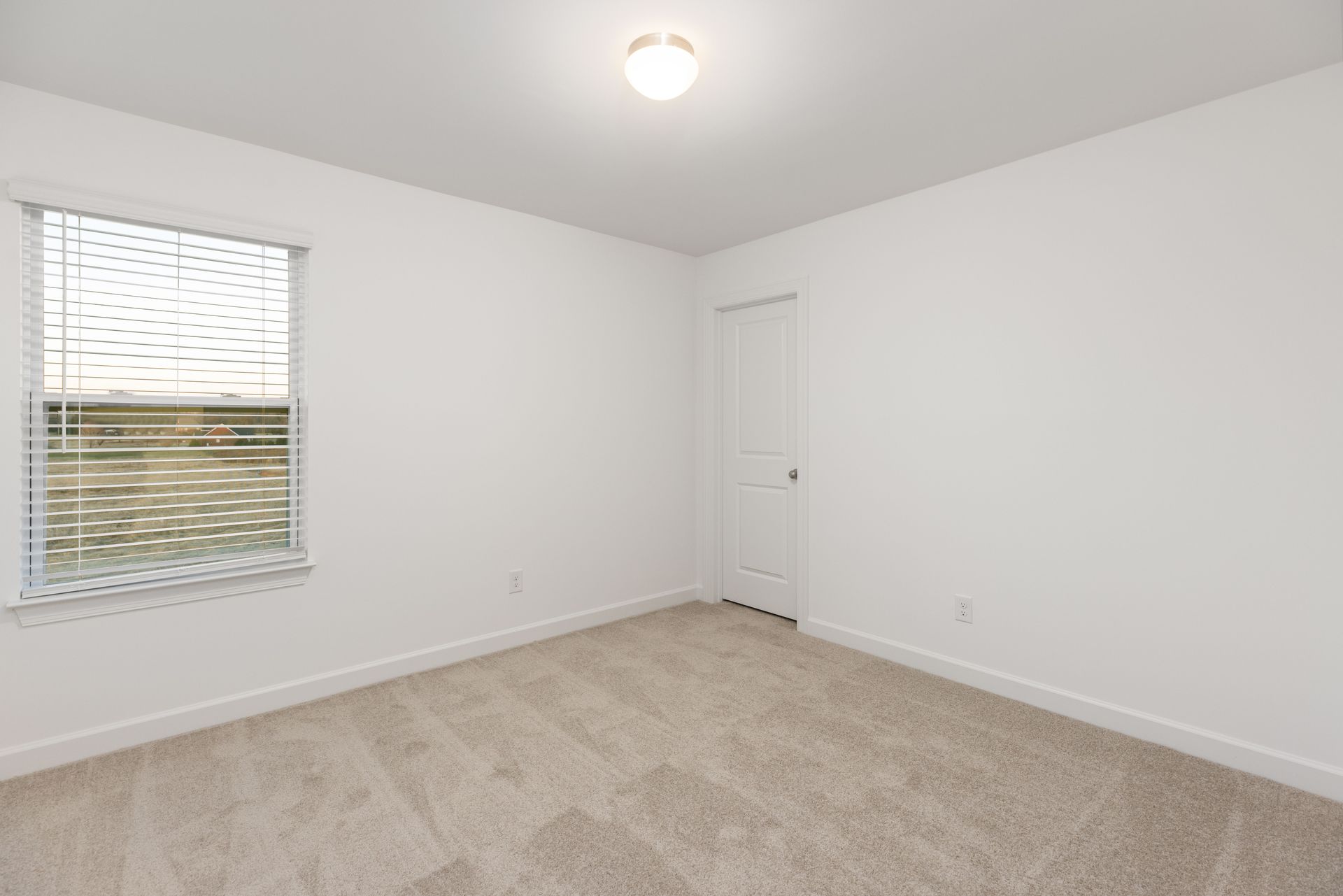 An empty bedroom with a window and a carpeted floor.