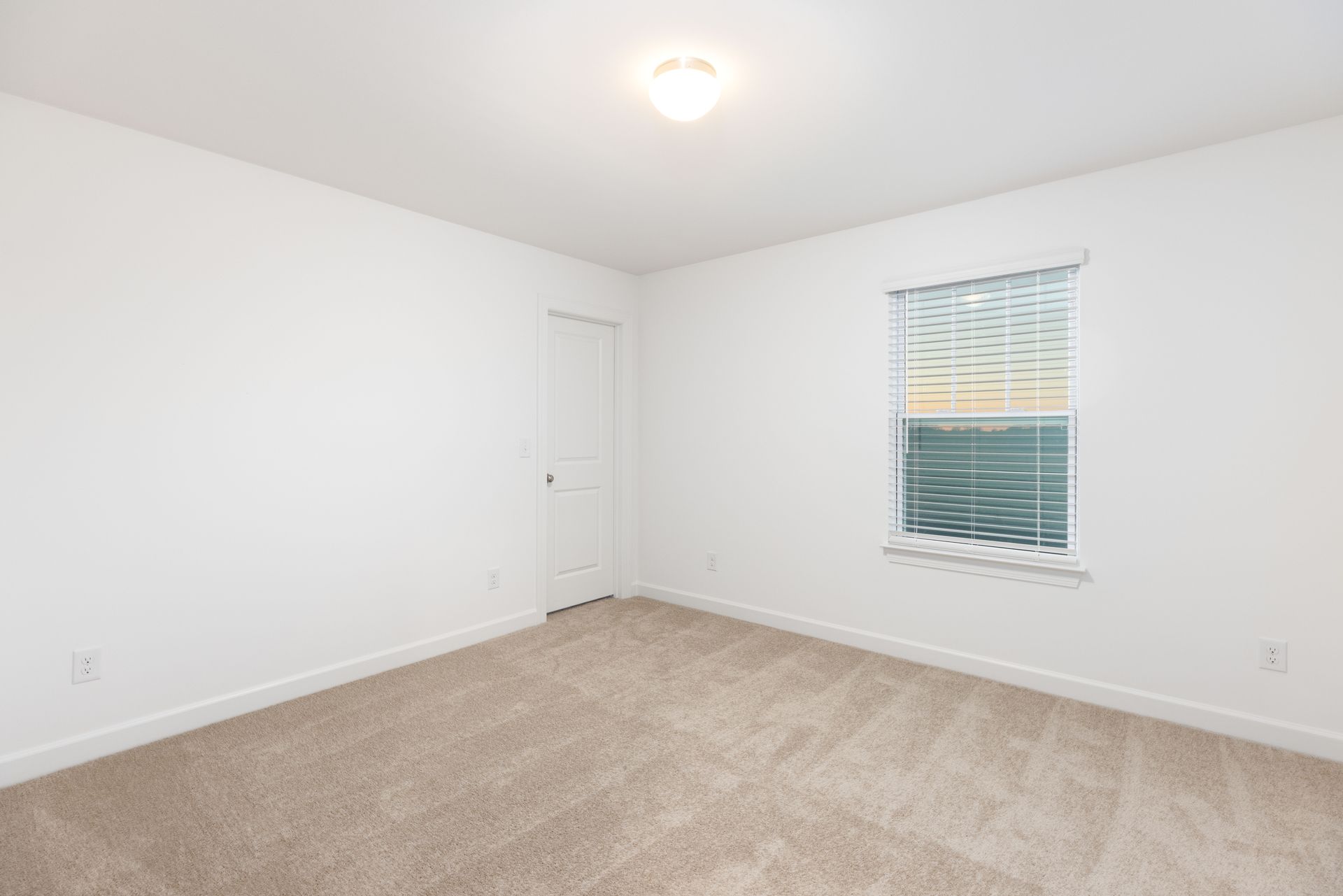 An empty bedroom with a window and a carpeted floor.