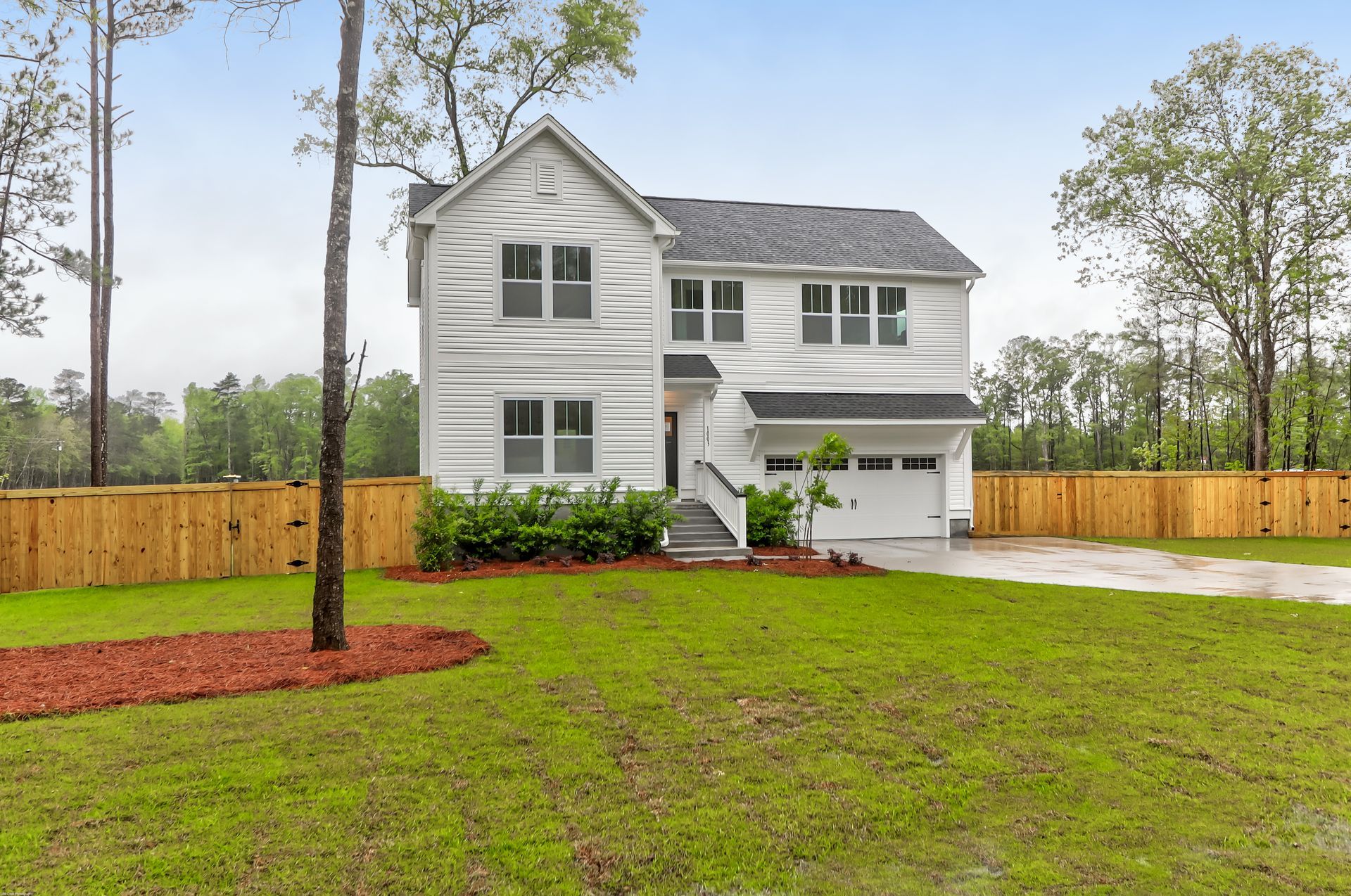 A white house with a wooden fence and a large lawn in front of it.