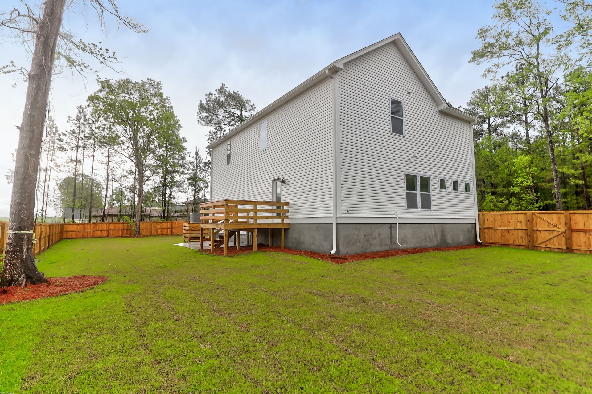 A large white house with a deck in the backyard surrounded by trees.
